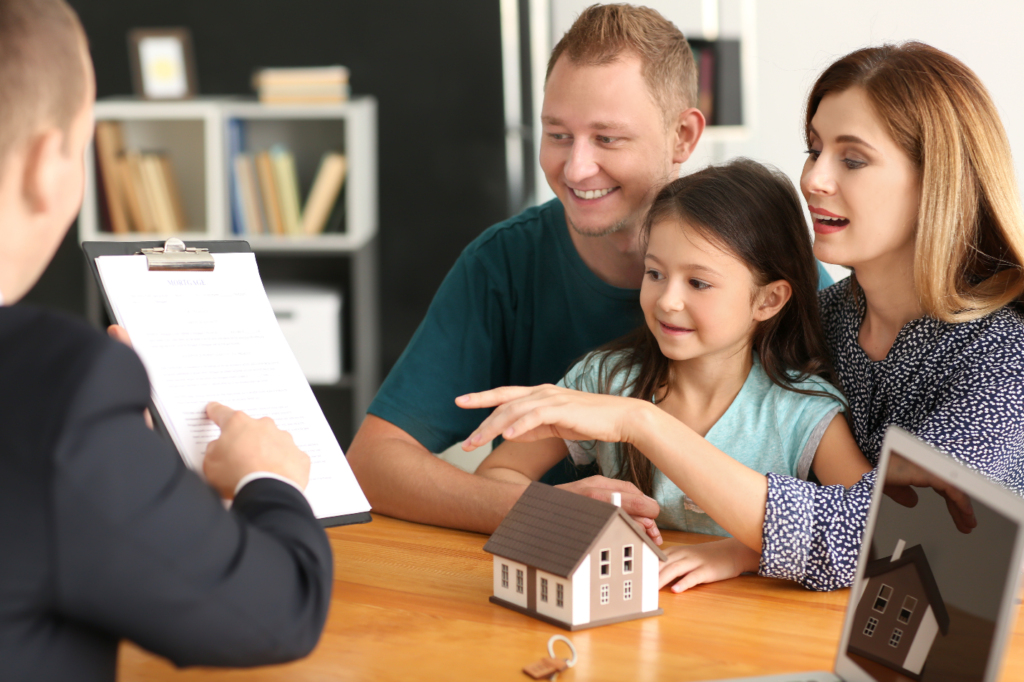 A family sitting at the table with a paper and a model house.