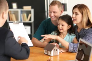 A family sitting at the table with a paper and a model house.